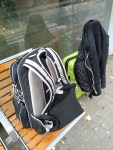 Rucksack und kleiner Koffer, über den eine schwarze Jacke gehängt ist, an einer Bushaltestelle
