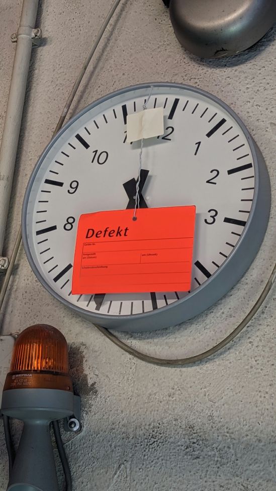 Wanduhr mit rotem aufgebrachten Zettel, auf dem DEFEKT steht.