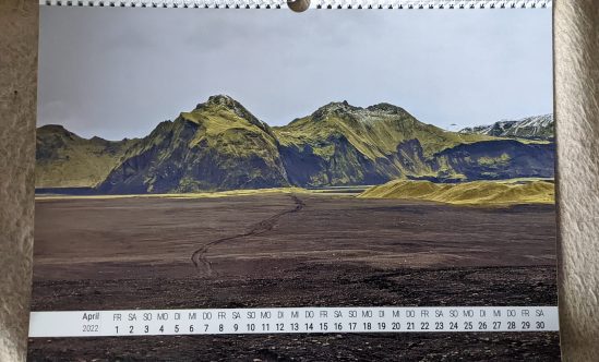 April Blick über eine braune Ebene, über die Reifenspuren führen, bis zu einem Berg im Hintergrund