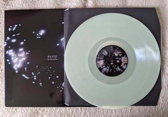 Plattencover von Hante "Her Fall And Rise " und weiß aussehender Vinyl-Platte (Ist aber "Glow in the Dark".)