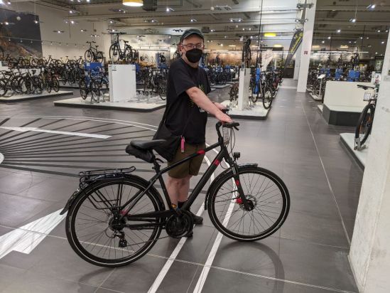 Ich mit dem erwähltem Typ von Rad im Fahrradladen - das Rad ist ein schwarzes Herrenrad mit roten Punkten.