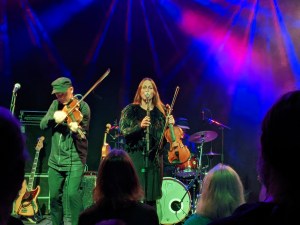Konzertfoto von GARMARNA im Schlachthof Wiesbaden am 15.09.2022 Emma Härdelin am Mikrofon, eine Violine samt Bogen in der linken Hand haltend, links daneben Stefan Brisland-Ferner Violine spielend
