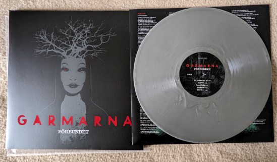 Plattenhülle und Vinylplatte in Silber von GARMARNA - Förbundet Auf dem schwrzen Cover ist der Kopf einer Frau mit roten Augen zu sehen, aus deren Kopf Äste eines Baumes wachsen