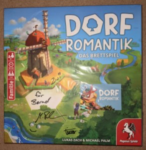 Spiel "Dorfromantik - Das Brettspiel" von Pegasus Spiele Auf der Verpackung ist eine große Windmühle zu sehen. Außerdem ist das Spiel signiert.