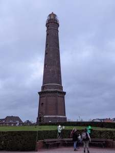 Neuer Leuchtturm im Hintergrund vorne stehen zwei Erwachsene mit 2 Kindern mit Laternen
