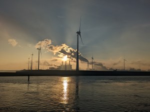 Die Sonne steht hinter Windrädern und den Abgaswolken der Eemshavener Industrie.