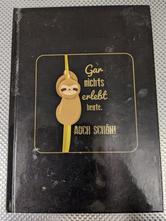 Notizbuch, auf dem ein Faultier abgebildet ist und daneben steht geschrieben: Gar nichts erlebt heute. AUCH SCHÖN!