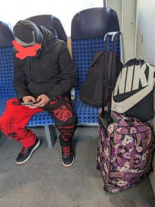3er Sitzgruppe in der Regionalbahn Ein Typ sitzt breitbeinig auf dem mittleren Platz, links neben sich sein Gepäck
