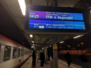 Ein Bahnsteig in der Nacht Auf der Anzeige steht RE59 04:23 Uhr über Maintal Ost - Frankfurt Ost - Frankfurt Süd - F-Stadion zum FFM Flughafen Regionalbahnhof weiter angeschrieben 04:54 Uhr RB 51 Frankfurt (M) Hbf und 04:17 Uhr (04:57 Uhr) IC 60471/471 Zürich HB / Ankunft Am Bahnsteig steht der Zug nach Zürich.