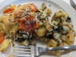 Kartoffel-Kohlrabi-Gratin mit Tomaten und Spinat und Sonnenblumenkernen auf Teller, samt Gabel
