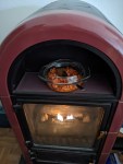Ein Gasofen, der aussieht wie ein Kaminofen mit Holz hinter einer Glasscheibe. Darüber ist eine Aussparung im Ofen, in der eine Glasschüssel mit Bohnen in Tomatenssoße steht