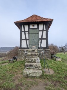 Das sogenannte Schützenhäuschen von Hochstadt - ein kleines Gebäude aus Fachwerk auf einem Steinsockel, zu dem eine Treppe mit Geländer führt