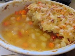 Auflaufform mit Kartoffel-Kohlrabi-Tomaten. Die eine Hälfte ist noch mit Käse überbacken, in der anderen Hälfte steht die Flüssigkeit, da noch zu flüssig