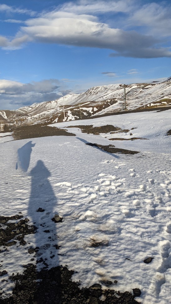 Berghänge und Schneefelder Auf dem Schnee direkt vor der Kamera sind drei Schatten zu sehen, aber keine Personen, die diese Schatten werfen. (Der mittlere Schatten ist der vom Fotografen.)