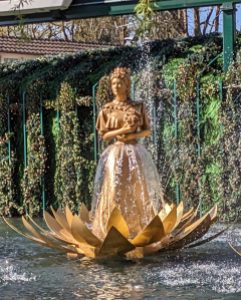 Eine goldene Sisi-Statue steht in einer goldenen Seerose auf dem Wasser und darum herum sind Wassertropfen von Fontänen zu erkennen. Auch der Rock ihres Kleides scheint aus Wasser zu bestehen.