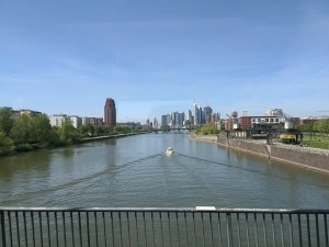 Skyline von Frankfurt vor blauem Himmel, im Vordergrund der Main mit einem kleinen Schiff.