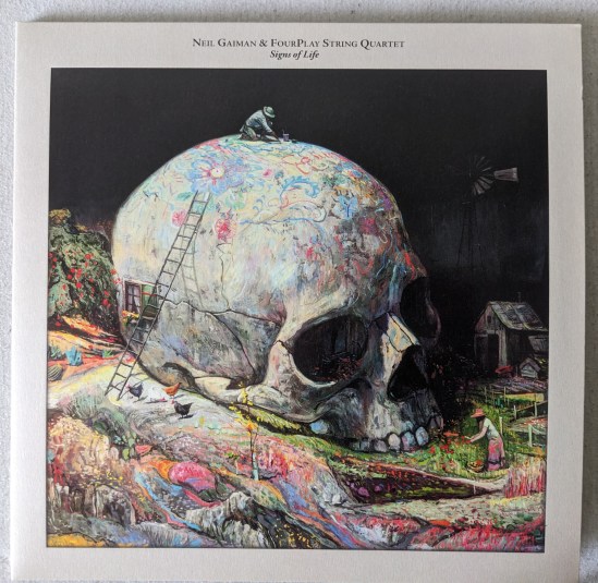 Cover der Platte Signs of Life von Neil Gaiman und dem FourPlay String Quartet. Zu sehen ist in Totenschädel, der bemalt ist auf ebenso bemaltem Boden An dem Schädel ist eine Leiter angelehnt. Auf dem Schädel malt ein Mann mit Hut, und hiter der Leiter ist ein Fenster mit Vorhängen im Schädel zu sehen. Vor der Leiter laufen drei Hühner herum. Rechts im dunkler werden Hintergrund steht ein Windrad über einer kleinen Hütte.