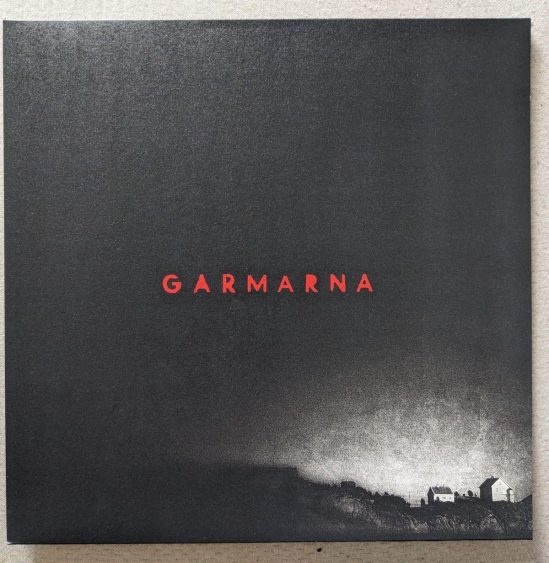 Cover der LP "6" von GARMARNA Rechts unten im Eck sind ein zwei Häuser vor hellem Hintergrund zu sehen, während der Rest der Seite Schwarz ist
