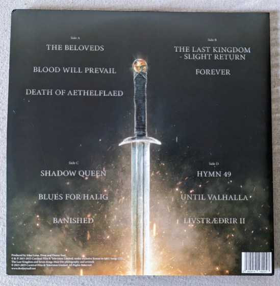 Rückseite des Covers vom THE LAST KINGDOM Ein Schwert steht im Feuer, so wie es scheint, da das Feuer grad außerhalb des Bildes ist, doch es sind die Funken zu sehen. Die Titel der Lieder sind auf der Rückseite geschrieben: Side A The Beloveds Blood will prevail Death of Aethelflaed Side B THE LAST KINGDOM - Slight Return Forever Side C Shadow Queen Blues for Halig Banished Side D Hymn 49 Until Valhalla Lívstræðrir II