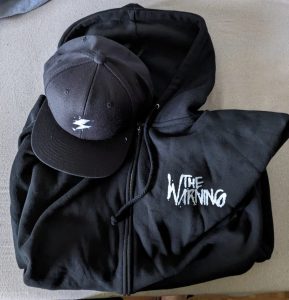 The Warning-Kappe mit Bitz-Symbol und Zipp-Hoodie mit der Aufschrift "The Warning" - beide in Schwarz