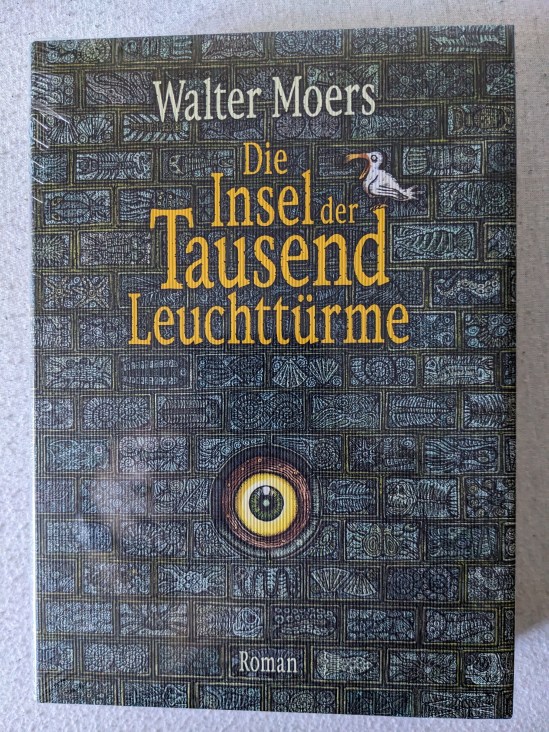 Buchtitel von Walter Moers: Die Insel der Tausend Leuchttürme zu sehen ist eine Mauer, in die ein Auge eingelassen ist