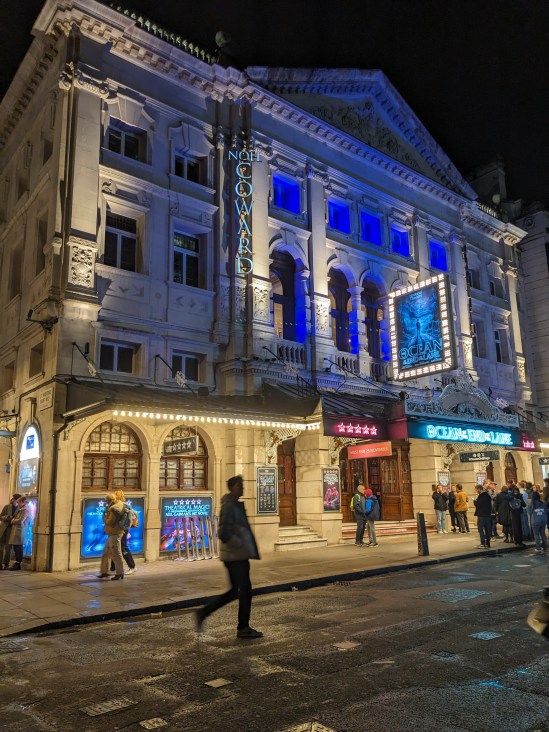 Das Noël Coward Theatre in London bei Nacht, beleuchtet. Zu sehen ist über dem Eingang die beleuchtete Anzeige von THE OCEAN AT THE END OF THE LANE