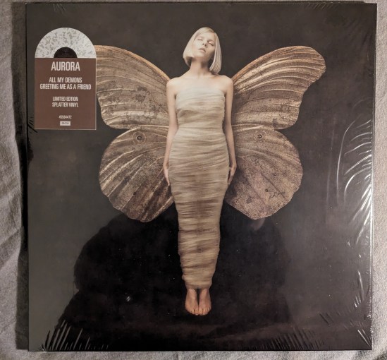 Cover der Platte von AURORA "ALL MY DEMONS GREETING ME AS A FRIEND" Aurora als Schmetterling/Motte mit Flügeln und den Körper noch quasi im Kokon.