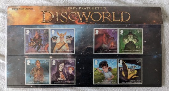 Briefmarken der Royal Mail Stamps von der Discworld PRESENTATIONS-PACK Auf den 8 Briefmarken sind zu sehen: RINCEWIND, MOIST (Feucht) VON LIPWIG, der BIBLIOTHEKAR, OMA WETTERWACHS samt MAGRAT und NANNY OGG, SAM VIMES, TOD und MORT, TIFFANY ACHING (Weh) und GREAT A'TUIN