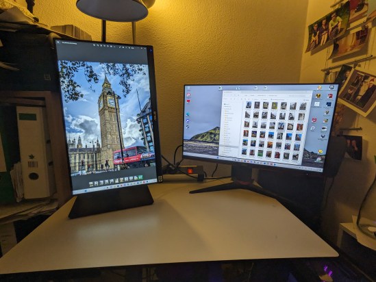 Beide Monitore sind an, wobei der neue Monitor links nun hochkant gestellt ist. Darauf ist der Big Ben zu sehen. Der rechte Monitor ist weiter horizontal, und da ist ein Ordner mit Fotos aus London zu sehen.