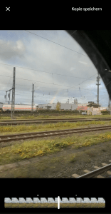 Screenshot des Fotos der Bahngleise und des Regenbogens. Darüber steht links ein X, rechts im Eck "Kopie speichern" und darunter sind die Bilder des Videos zu sehen mit einem Strich, welches Bild gerade gezeigt wird.