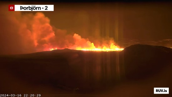 Bildschirmfoto der Eruption vom 16.03.2024 Livestream von RÚV. Unten links steht 2024-03-16 22:20:29 Oben links im Eck steht die Standortangabe der Kamera: Þorbjörn - 2 Im Vordergrund ist die dunkle Linie von Erhebungen vor einer brennenden Fläche mit großer Qualmentwicklung zu sehen. Unten rechts steht RUV.is