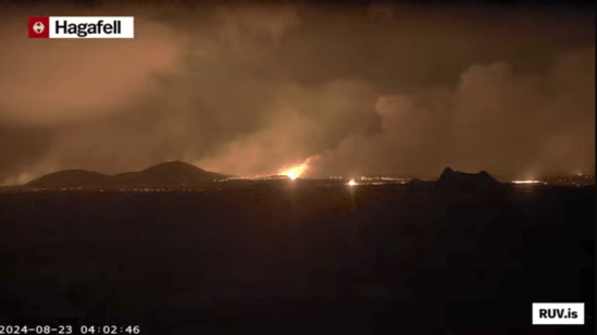 Bildschirmfoto der Eruption vom 22.08.2024 Livestream von RÚV. Unten links steht 2024-08-23 04:02:46 Oben links im Eck steht die Standortangabe der Kamera: Hagafell Es ist Nacht. In der Bildschirmmitte ist der Eruptionsschein zu sehen. Rechts davon ist einer der alten Krater zu erkennen. Der von der Eruption beleuchtete Himmel ist voller Qualm. Unten rechts steht RUV.is