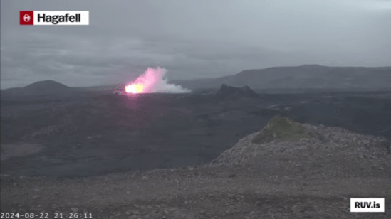 Bildschirmfoto der Eruption vom 22.08.2024 Livestream von RÚV. Unten links steht 2024-08-22 21:26:11 Oben links im Eck steht die Standortangabe der Kamera: Hagafell Etwas links von der Bildschirmmitte beginnt gerade die neue Eruption. Rechts davon ist einer der Krater von einer der vorherigen Eruptionen zu sehen. Unten rechts steht RUV.is