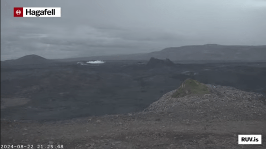 Bildschirmfoto der Eruption vom 22.08.2024 Livestream von RÚV. Unten links steht 2024-08-22 21:25:48 Oben links im Eck steht die Standortangabe der Kamera: Hagafell Etwas links von der Bildschirmmitte ist Qualm am Boden zu erkennen, wo gleich das Feuer der neuen Eruption erscheinen wird. Rechts davon ist einer der Krater von einer der vorherigen Eruptionen zu sehen. Unten rechts steht RUV.is