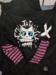Rückseite einer Jinx-Kapuzenjacke Grundfarbe ist Schwarz, auf der Rückseite ein großer Affentotenkopf im Jinx-Style Die Ärmel sind lila-scharz gestreift, rechts oben ist ein großes weißes Kreuz, unten ein Smiley.