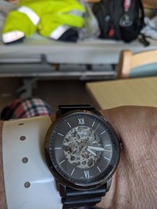 Blick auf die Armbanduhr, Uhrzeit 16 Uhr 17 Minuten. Im unscharfen Hintergrund ist ein Bett zu sehen, auf dem meine gelbe Arbeitsjacke und mein Rucksack zu erkennen ist.