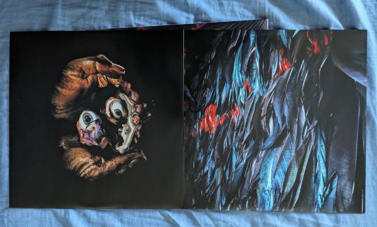 Innenhüllen der Vinyl-Platten des Albums Tangaroa von der Band Alien Weaponry Das eine Innencover ist vor einem schwarzen Hintergrund zwei Hände, die Augen halten. Das andere könnten blaue Fdedern oder Blätter sein.