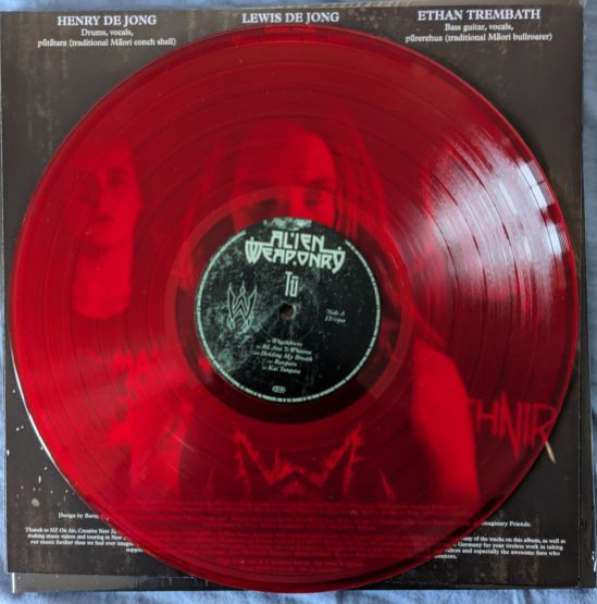 Transparent-rote Vinylscheibe des Albums Tū von der Band Alien Weaponry Durch die Platte sind die Mitglieder der Band zu erkennen.