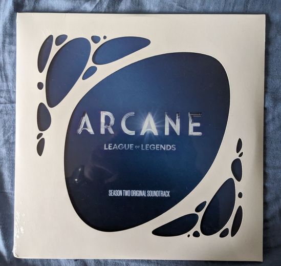 Cover zum Soundtrack ARCANE League of Legends Season Two Das Cover ist weiß, mit blauen Flecken. In dem Fleck in der Mitte steht der Titel.