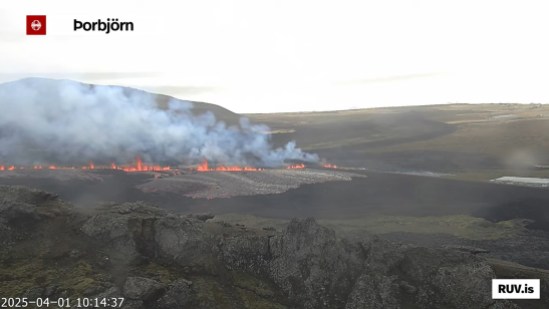 Bildschirmfoto der Eruption vom 01.04.2025 Livestream von RÚV. Unten links steht 2025-04-01 10:14:37 Oben links im Eck steht die Standortangabe der Kamera: Þorbjörn Im Hintergrund ist das sonnenbeschienene Meer zu sehen. Auf dem Land davor zieht sich eine Feuerlinie in der Mitte des Bildes bis etwa zur Mitte. Vor dieser Feuerlinie ist die sich ausbreitende Lava-Fläche zu erkennen. Von links nach rechts zieht sich der Verteidigungswall von Grindavík, der die Feuerlinie zu unterbrechen scheint, allerdings ist auf beiden Seiten des Walls Feuer zu sehen. Unten rechts steht RUV.is