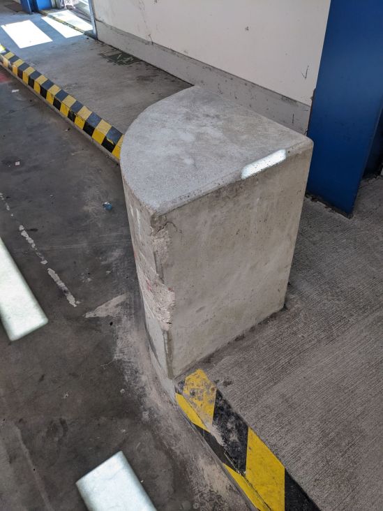 Ein Betonpoller schütze eine Ecke, die Form ist wie ein Viertelstück von einem hohem runden Kuchen