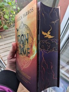 Buch mit Farbschnitt (einem fliegenden goldenen Drachen über Gewitterwolken) Das Buch ist das Hardcover von Iron Flame - Flammengeküsst von Rebecca Yarros.