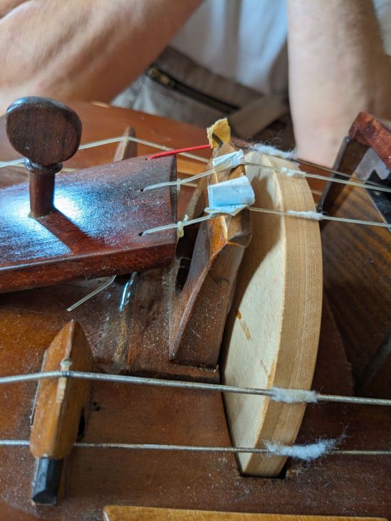 Melodiesteg von Drehleier, unter die Saiten sind Papierstücke geklemmt