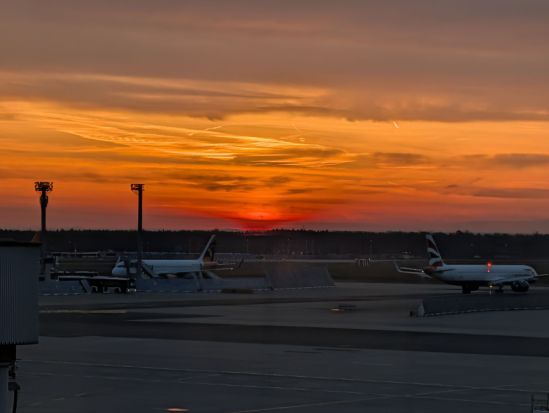 Blick auf Flughafen-Rollfeld kurz vor Sonnenaufgang, der sich tiefrot ankündigt.